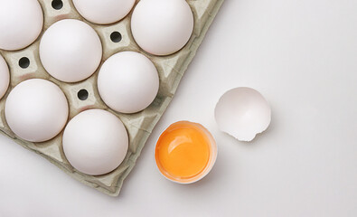 Fresh white chicken eggs in carton box and egg half with a yolk on white table. Top view.