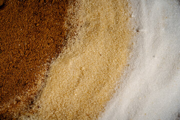 Fototapeta na wymiar trois variétés de sucre différents étalés sur une table, en macro, blanc, bruns, roux