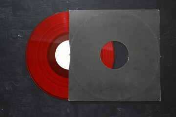 Aged black paper cover and red vinyl LP record isolated on stone background 
