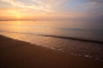 Calm sea shore with crushing waves on sandy beach at sunrise