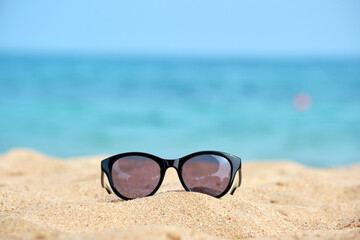 Closeup of black protective sunglasses on sandy beach at tropical seaside on warm sunny day. Summer...