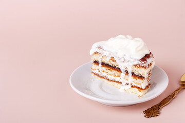 one piece of tiramisu with dripping cream lies on a plate, a spoon on a pink background with copy space
