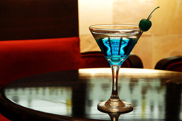 Martini cocktail with olive on wooden bar table in warm atmosphere with space for text