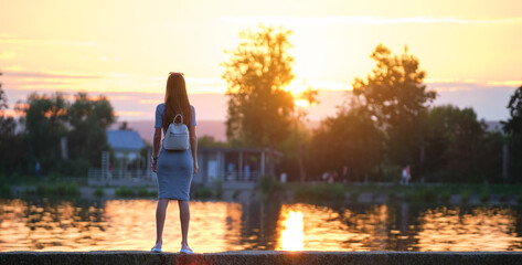 Back view of lonely woman standing on lake side on warm evening. Solitude and relaxation concept