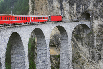 Passenger train goes from Chur to St. Moritz on Landwasser viaduct.
