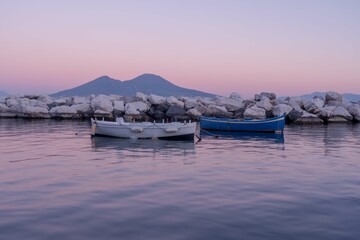 Tiny boates are docked in a calm port, in background Vesuvius