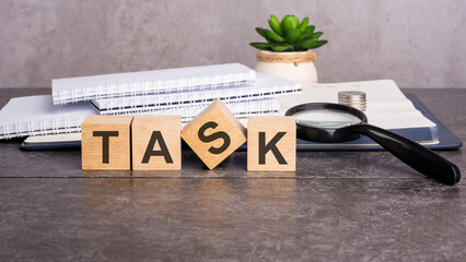the word Task is written on wooden cubes on a gray background. close-up of wooden elements, magnifying glass, paper documents