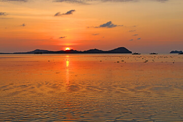 Rippling sand during low tide at the beach with background of islands and fishing boats with sun reflecting on the sea in Quezon, Palawan, Philippines