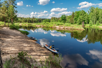 Naklejka premium View from high bank to forest river and two kayaks near shore