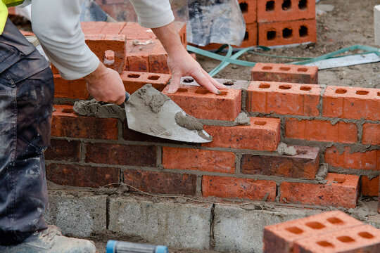 Bricklayer laying bricks on mortar on new residential house construction site