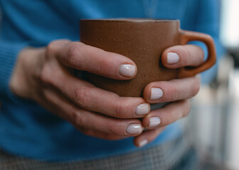 hands of woman in blue sweater holding brown cup of coffee or hot chocolate in the cafe Cold hand warm mug