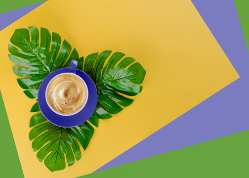 very pery  cup of coffee on a large green leaves on a yellow, purple and green background