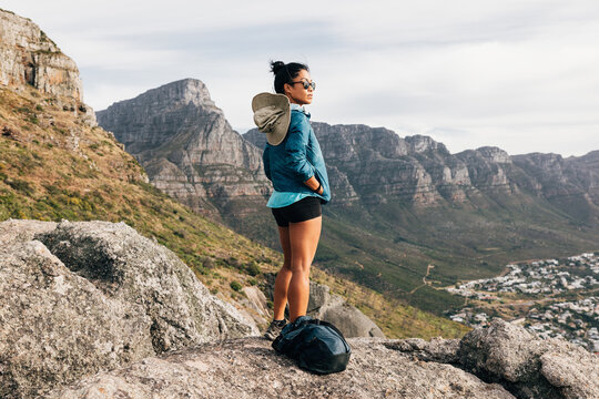 Young woman in sport clothes with backpack looking at the view while standing on a cliff