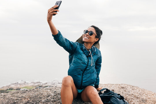 Happy woman making selfie while sitting on a rock. Positive female hiker relaxing during an adventure.