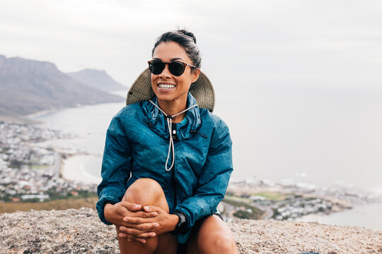 Smiling woman wearing sunglasses relaxing during hiking sitting on a rock
