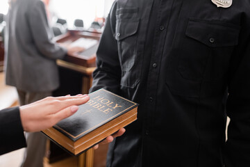 partial view of bailiff holding bible near woman giving swear in court