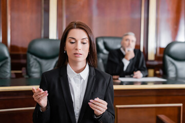 brunette prosecutor pointing with finger during speech in courtroom near judge on background