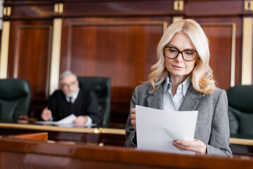 middle aged advocate in eyeglasses reading document while speaking in court