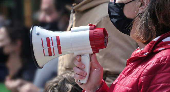 Mulher a falar atrav&eacute;s de um megafone no meio de uma multid&atilde;o, manifesta&ccedil;&atilde;o, m&atilde;o a segurar no megafone, m&aacute;scara na cara, pandemia, COVID-19