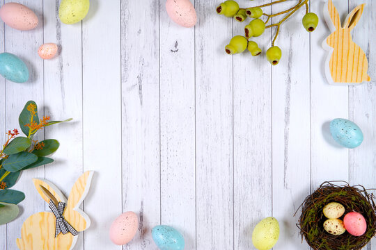 Happy Easter flatlay farmhouse framed border backdrop styled with wood bunnies, and pastel eggs against a white wood background. Negative copy space.
