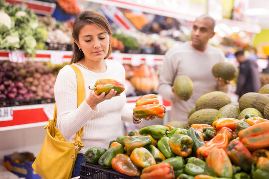 Positive woman picking ripe bell peppers at grocery supermarket