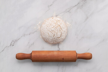 Fresh homemade yeast dough resting on marble table with ears of wheat and rolling pin.