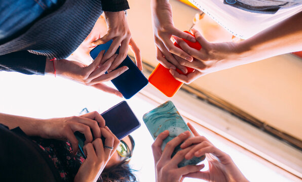 Diverse View from below of young women hands standing together holding smartphones