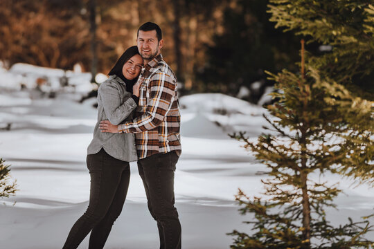Beautiful couple hugging between snowy pines, woman in casual clothes holding hands on man chest. Selective focus
