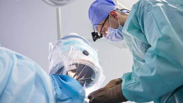 Surgeon sewing the patient at the end of surgery. Doctor bent over the patient at operation. Low angle view.