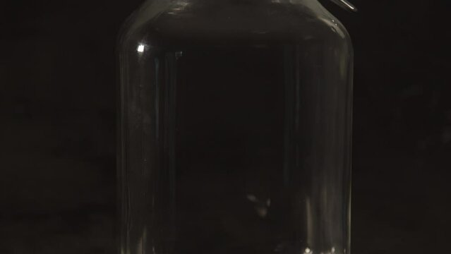 Tilt down of glass preserving weck jar with metal bracket against a black background