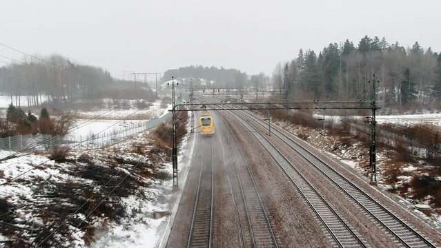 Aerial shot of a speed train, Arlanda Express passing by under drone in industrial, winter landscape going towards Stockholm City Terminal.