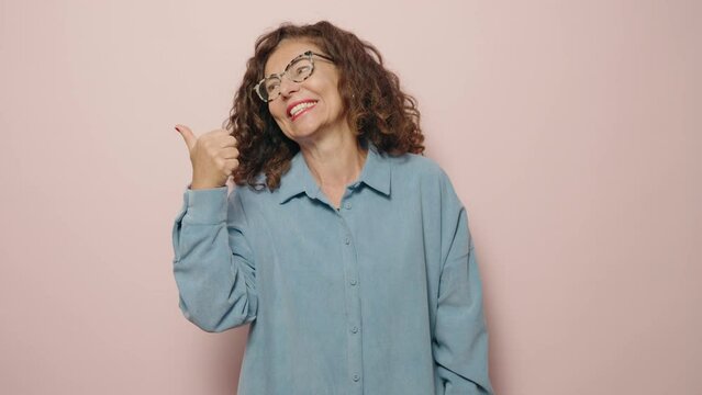 Middle age woman smiling confident pointing with fingers to the side over pink background