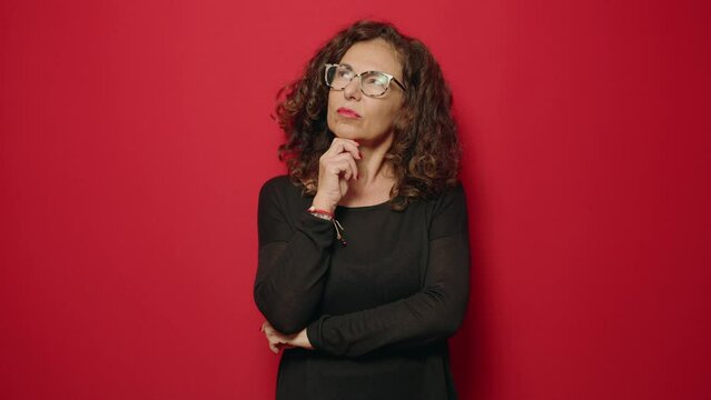 Middle age woman with thinking gesture standing over red background