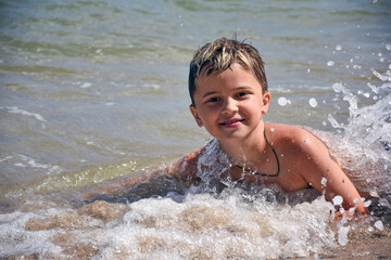 White race teenager boy bathes in the sea in waves and spray and smiles