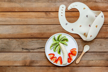 Creative meal for a child, strawberries and banana, funny food over wooden background. Fruits for baby. Top view, flat lay