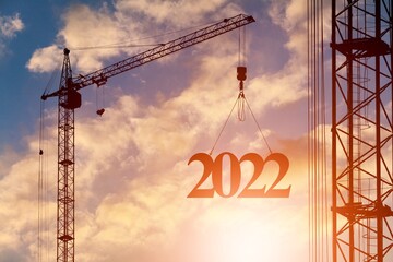 Silhouette of a construction crane at a construction site raising the number 2022 year. Concept for New Year for development and business