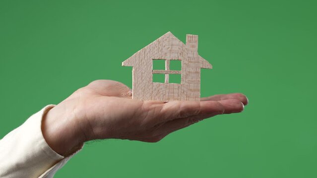Concept of hand holding wood cutout of house on green screen chroma key background.