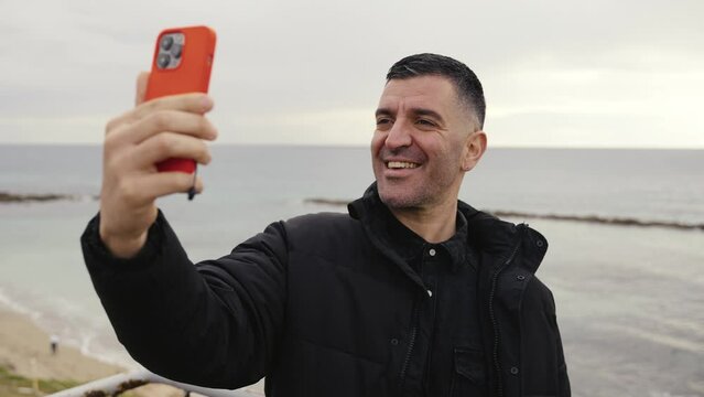 A man has fun and makes a silly face while taking selfies and creating social media stories while on the beach.