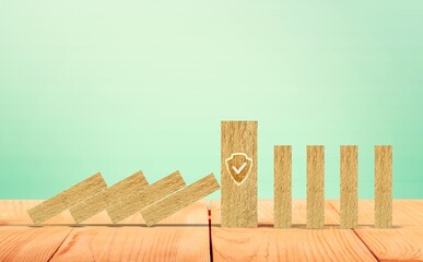 The wooden block strong with shield security icon symbol standing protects falling domino pieces