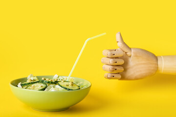 Wooden hand showing thumb-up and bowl of healthy salad on yellow background