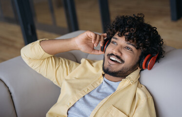 Portrait of young smiling Indian man using wireless headphones listening music relaxing at home....