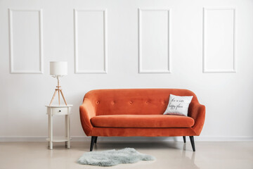 Stylish brown sofa and table with lamp near light wall