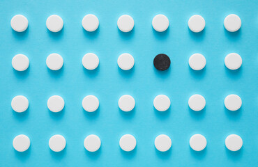 Black pill among white ones on blue background. Concept of uniqueness