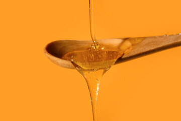 Honey dripping into wooden spoon on color background, closeup