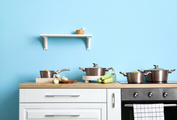 Cooking pots, vegetables on wooden table and shelf with mortar near color wall