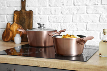 Cooking pots with prepared food on stove near white brick wall