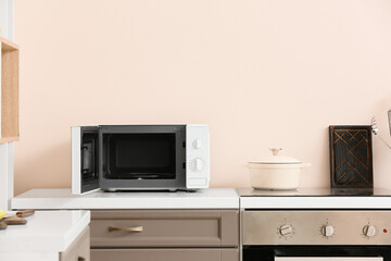Opened microwave oven on counter near light wall in kitchen - obrazy, fototapety, plakaty