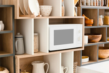 Shelf unit with kitchenware and modern microwave oven
