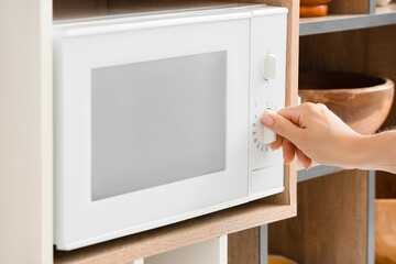 Young woman using microwave oven on shelf unit in kitchen, closeup