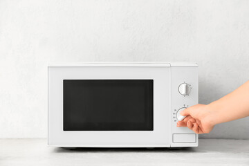 Woman heating food in microwave oven on light background, closeup